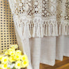Beige sheer curtain with lace trim and tassel fringe hanging in a light-colored fabric drape.