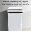 A white touchless motion sensor trash can with a black lid standing on a light surface.