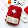 A red pouch with a white cross and a beige pocket is shown next to various first-aid supplies.