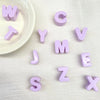 Perles en acrylique violettes formant l'alphabet éparpillées sur une surface blanche à côté d'un petit plat