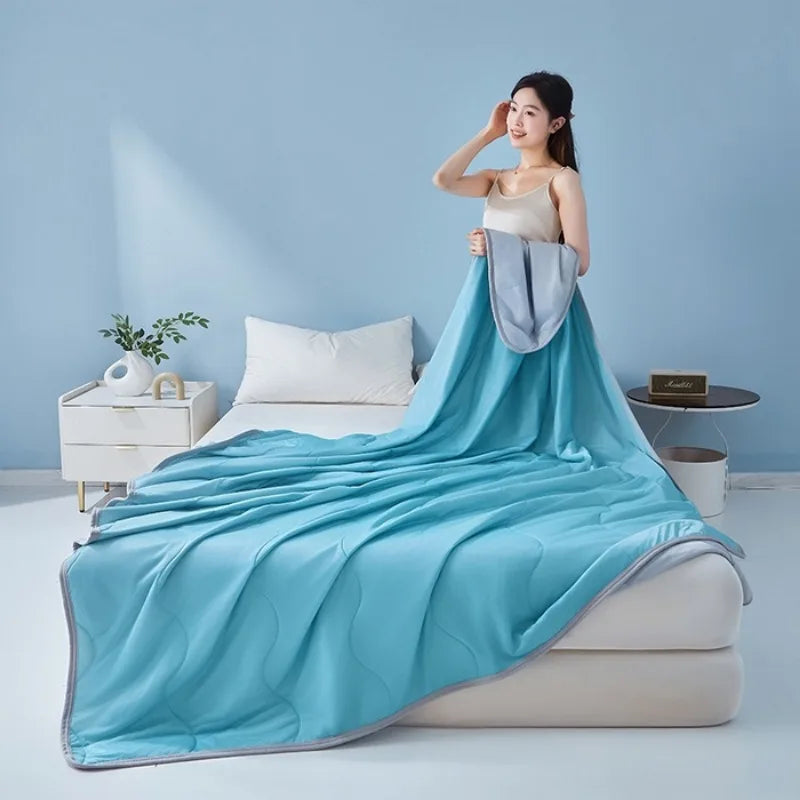 A woman models a light blue cooling summer quilt draped over a bed in a bright room.