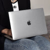 A person holds a silver Apple MacBook laptop with a protective case, resting on their lap.