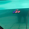 A close-up of a green vehicle body featuring a 3D tri-color grille emblem sticker with American and European flags.