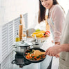 A person is cooking in a pan on a stovetop, with a foldable aluminum stove splatter guard visible.