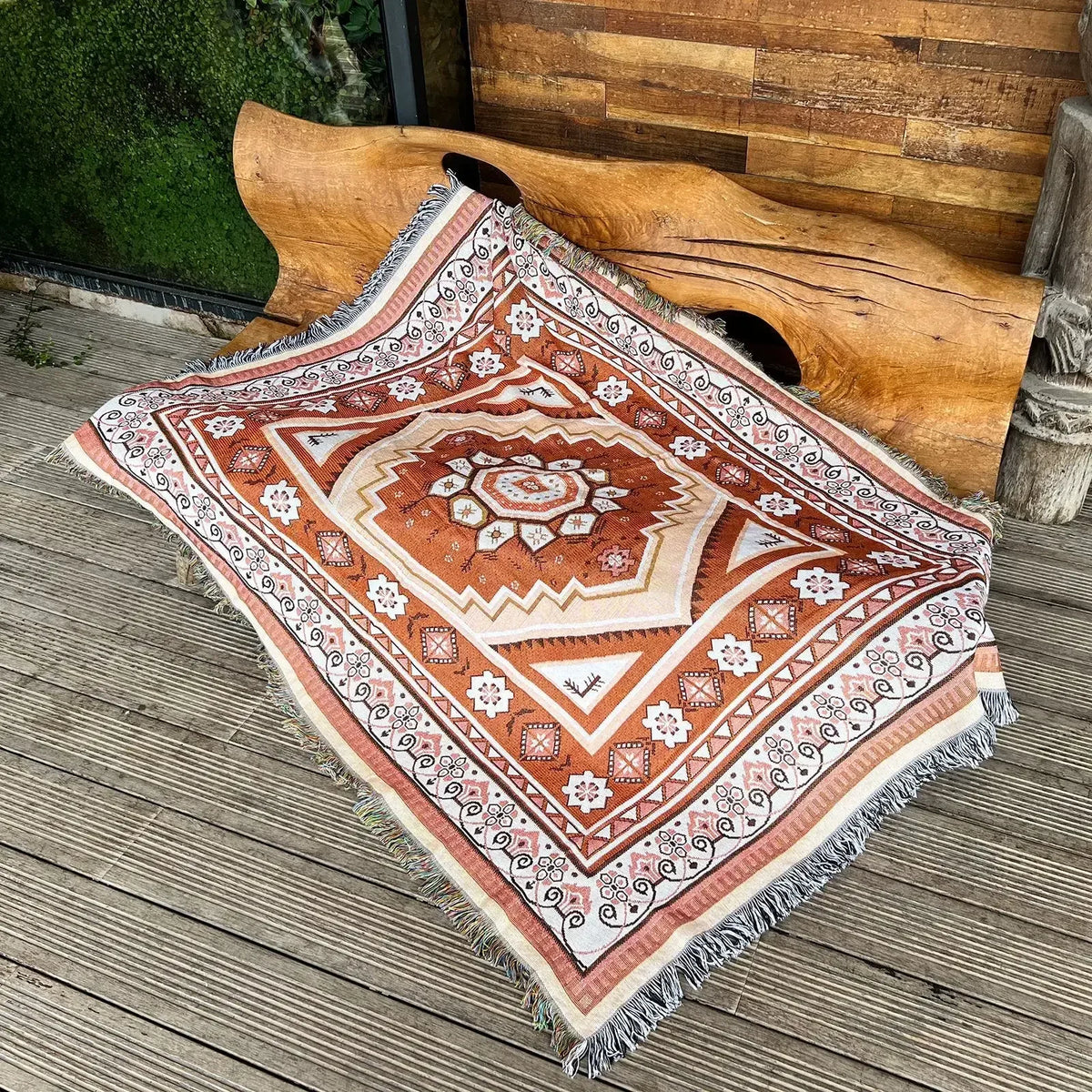 A patterned bohemian jacquard woven throw blanket with geometric designs laid on a wooden deck next to a large wooden carving
