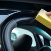 A yellow plastic and leather care product is being applied to a car interior surface.