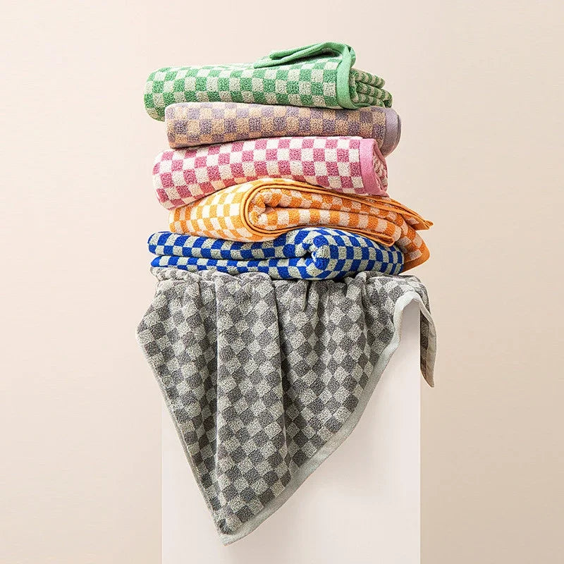 A stack of soft plaid cotton bath towels in various colors including green, purple, pink, orange, and blue.