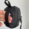 A hand holds a black plaid utility pouch with a strap and clip.