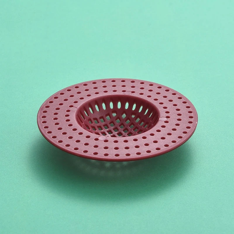 A round, pink silicone sink drain filter strainer with a grid pattern.