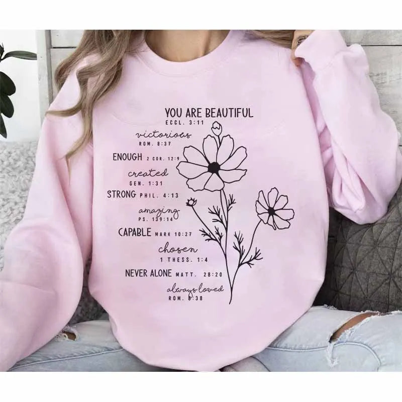 Pink sweatshirt featuring black script text about being beautiful and strong with a floral design