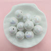 A white oval dish holds a collection of iridescent, spherical acrylic beads for jewelry making.