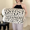 A woman models a white and black leopard print plush jacquard throw blanket draped over her arm.