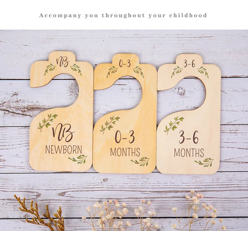 A set of eight wooden baby closet dividers for organizing clothes, labeled with age ranges from newborn to 3-6 months.