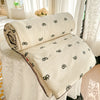 A cream-colored lightweight quilt with a subtle black pastoral print is rolled and folded on a white draped surface.
