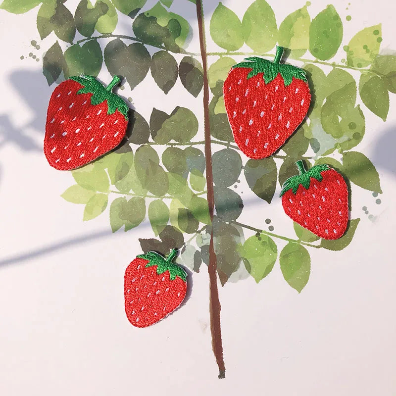A red strawberry embroidery patch is placed on a green leaf background.