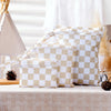 A set of four beige and white checkered reusable waterproof wet bags displayed on a table.
