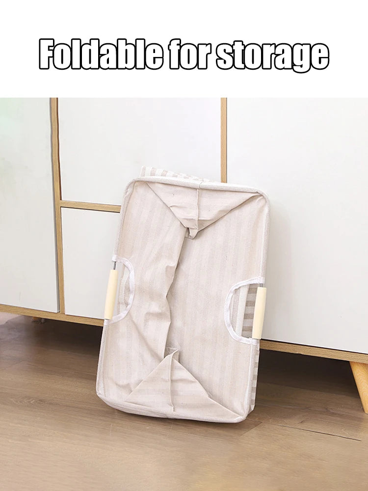 A beige foldable laundry basket with handles is shown standing on a wooden floor.