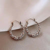 Pair of gold finish twisted zircon hoop earrings displayed on a neutral fabric background.