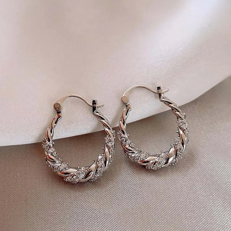 Pair of gold finish twisted zircon hoop earrings displayed on a neutral fabric background.