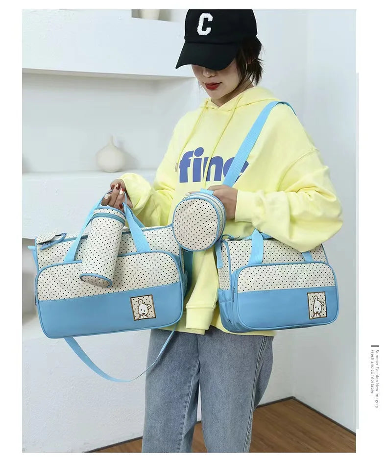 A woman wearing a yellow hoodie holds a light blue multifunctional crossbody diaper bag set.