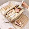A beige cosmetic bag is open, displaying various makeup and skincare products like lipsticks and foundations on a white marbl