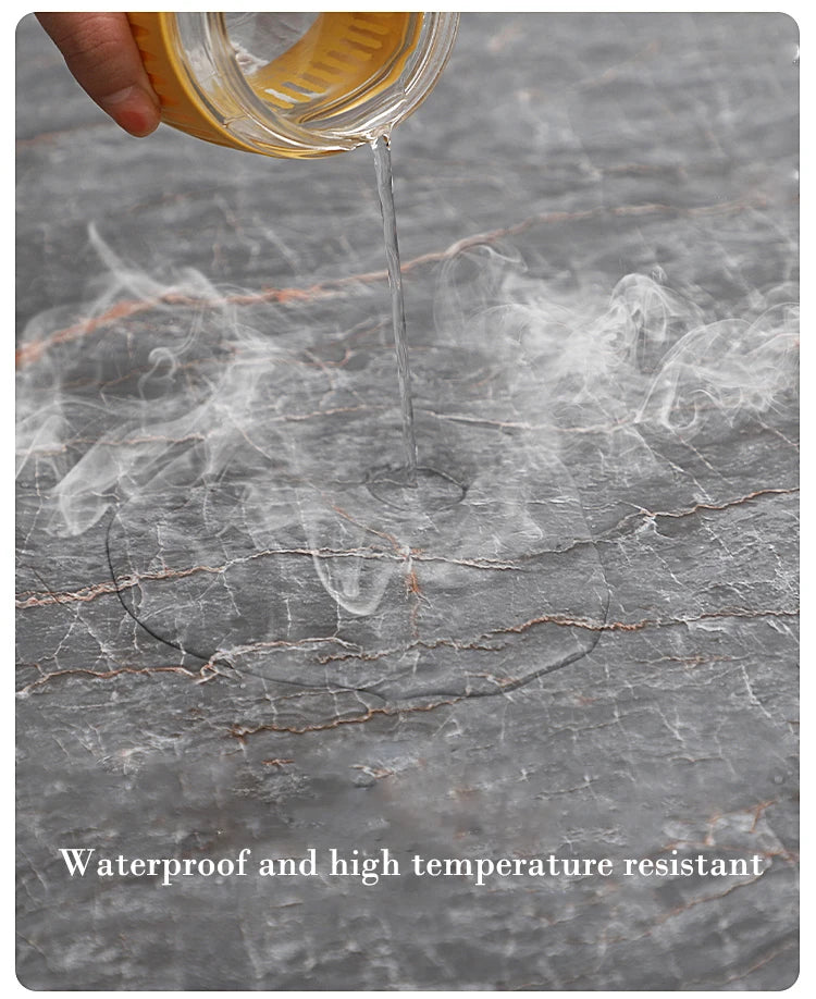 A hand pours liquid from a glass container onto a gray marble-effect surface, creating wisps of steam.