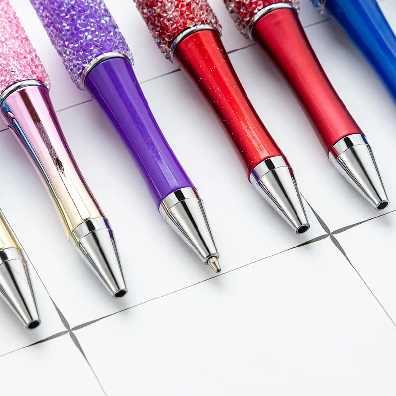 A close-up view of a set of ten colorful, glittery beaded ballpoint pens arranged diagonally on a white surface.