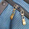 A close-up of a brass metal zipper pull replacement slider attached to a dark fabric strap.