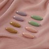 A set of eight oval solid color scarf pins in shades of lavender, mint green, yellow, and pink resting on a pink fabric.