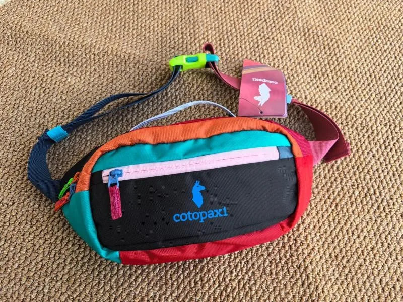 A colorful unisex water-resistant crossbody chest bag with orange, pink, and black panels resting on a tan fabric surface.