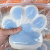A hand is squeezing a white and light blue soft sticky cat paw squeeze toy for stress relief.