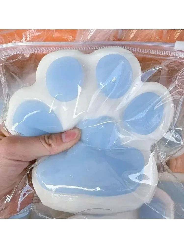 A hand is squeezing a white and light blue soft sticky cat paw squeeze toy for stress relief.