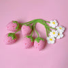Handmade crochet strawberry car mirror pendant with green stems and white flowers on a pink background