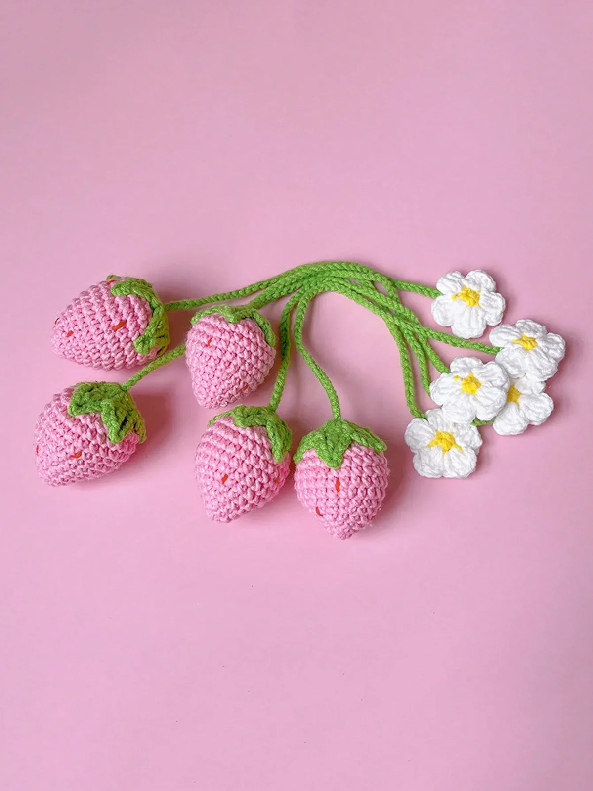 Handmade crochet strawberry car mirror pendant with green stems and white flowers on a pink background