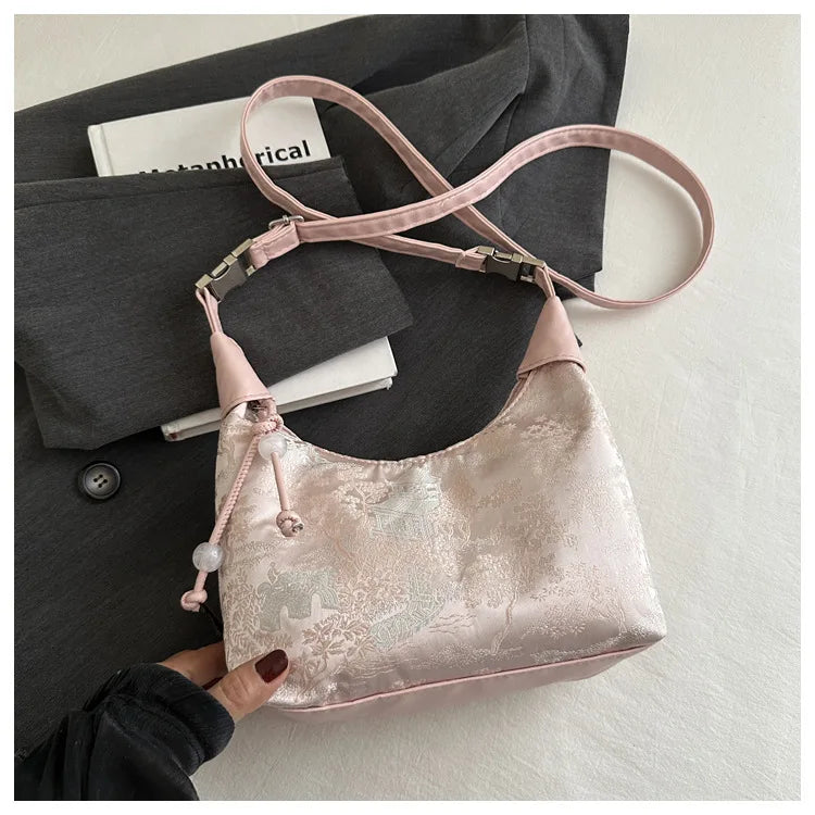 Hellrosa Satin-Crossbodytasche mit Perlenstickerei vor grauem Blazer und weißem Buch