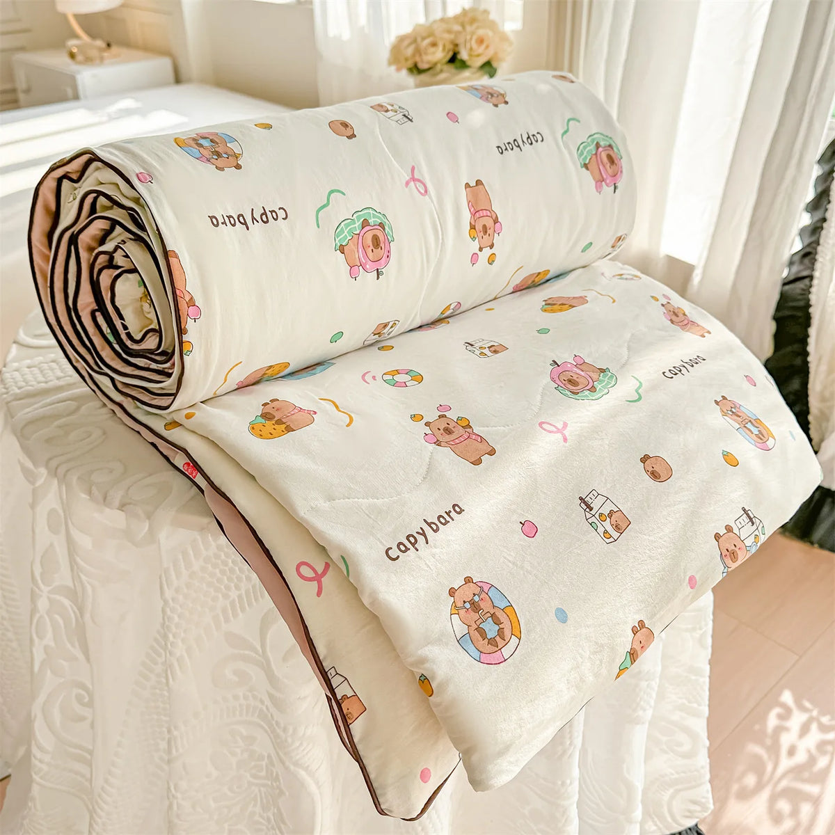 A rolled and unfolded cream-colored quilt featuring a pastoral print design with cute animal characters.