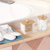 A set of cotton swabs and a glass organizer with a wooden lid placed on a bathroom counter.