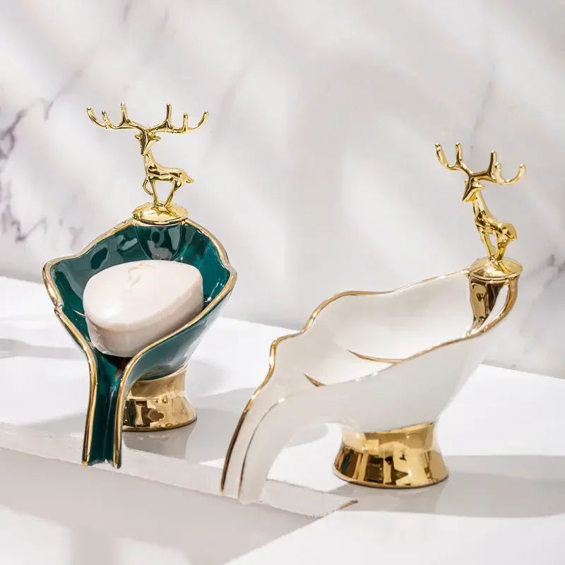 A white ceramic soap dish shaped like a leaf with a gold drain rack, set against a light background.