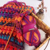 A ball of gradient dyed wool blend yarn in vibrant colors is shown next to wooden knitting needles and a woven basket.