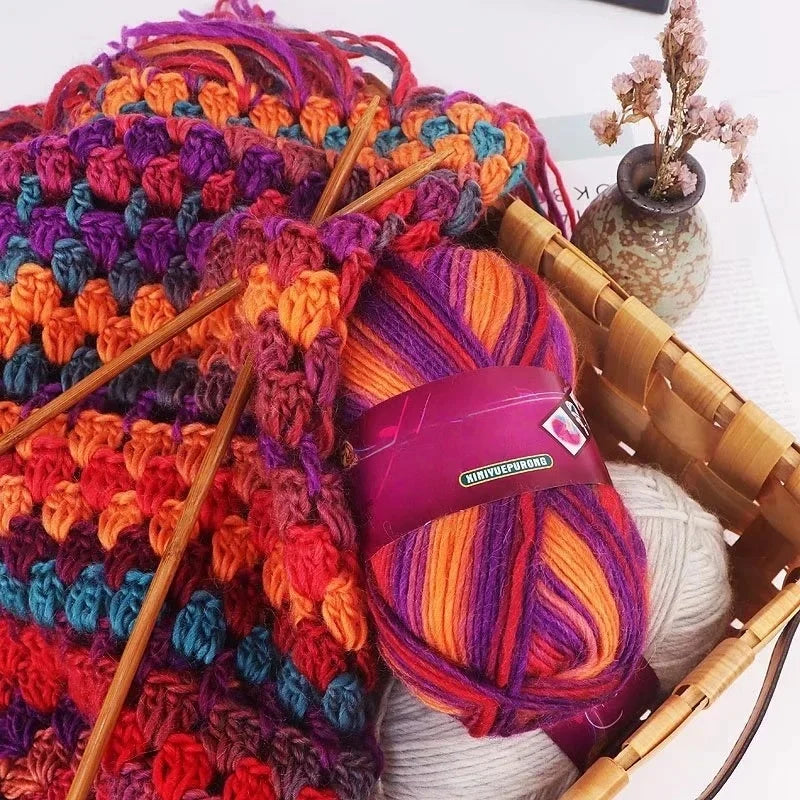 A ball of gradient dyed wool blend yarn in vibrant colors is shown next to wooden knitting needles and a woven basket.