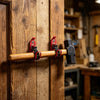 A wooden shovel holder with red hooks is mounted on a vertical wooden plank.