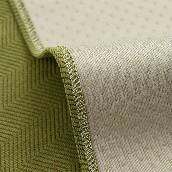 Close-up of a beige chenille textured non-slip sofa cover with a green quilted edge.
