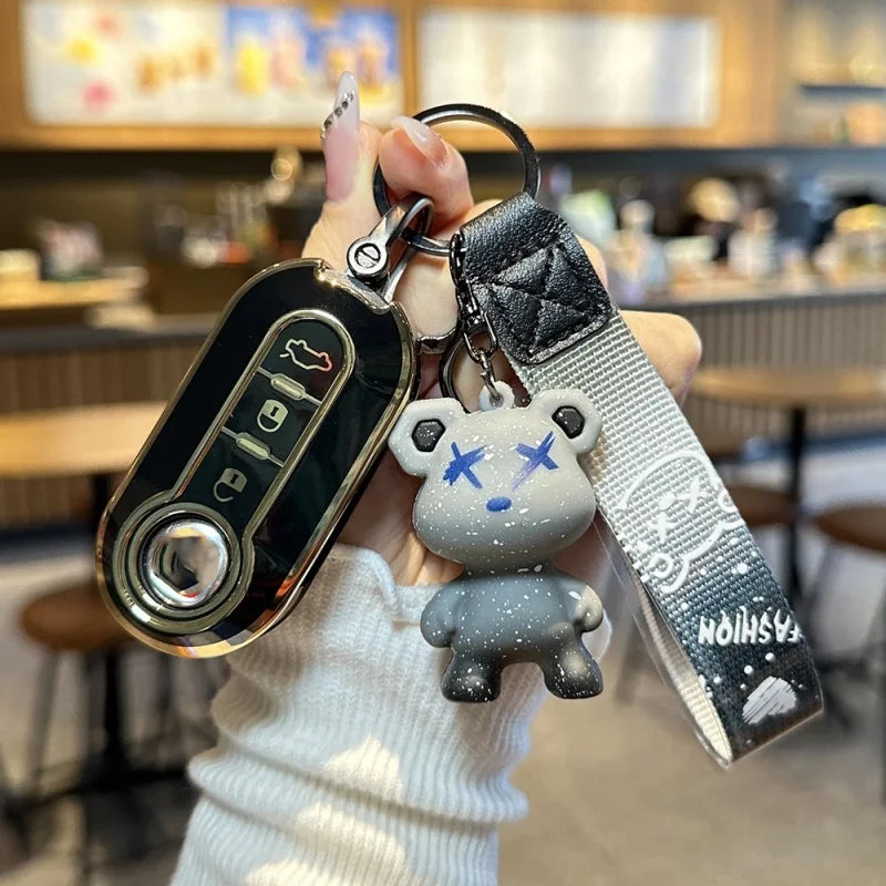 A hand holds a luxury leather key case keychain featuring a bear charm and a metal fob.