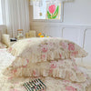 A set of two floral cotton pillowcases with pink and green roses resting on a white bed.