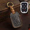 A dark brown leather key fob case with a brass ring attached, resting on a dark surface next to a white electronic fob.