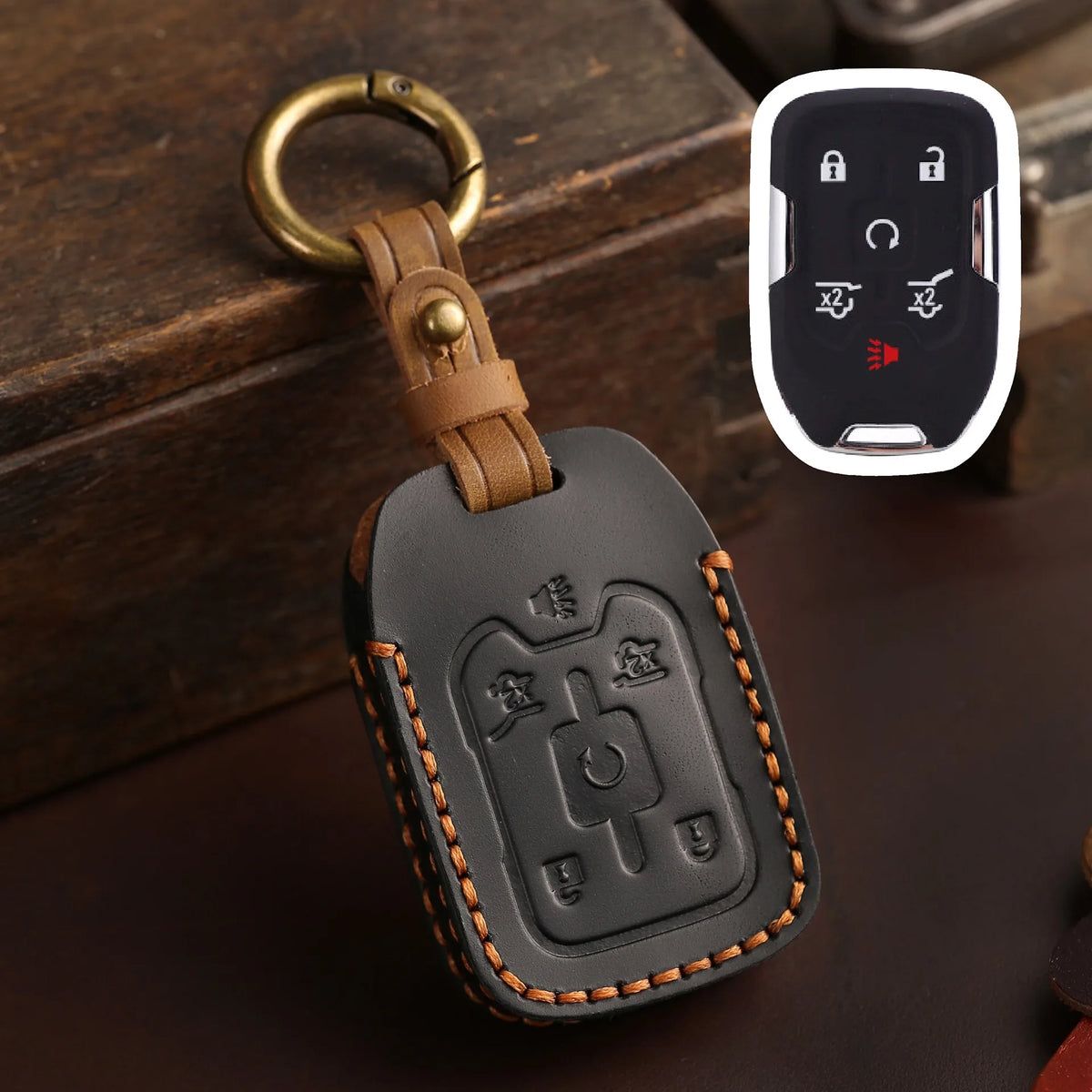 A dark brown leather key fob case with a brass ring attached, resting on a dark surface next to a white electronic fob.