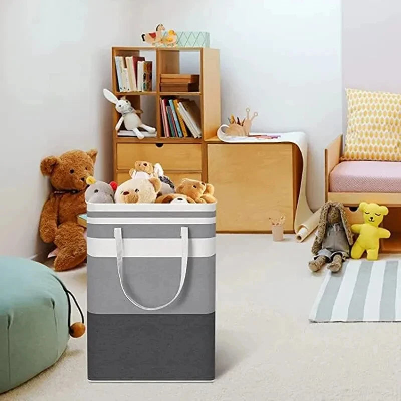 A large gray and white foldable canvas laundry basket stands next to a wooden shelf unit in a bright room.