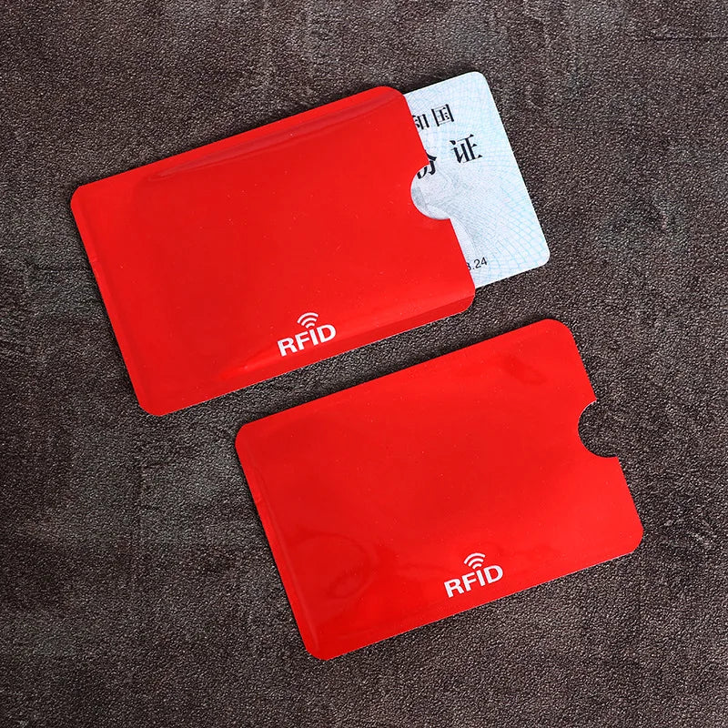 A set of red RFID blocking card sleeves and a white identification card are displayed on a dark surface.