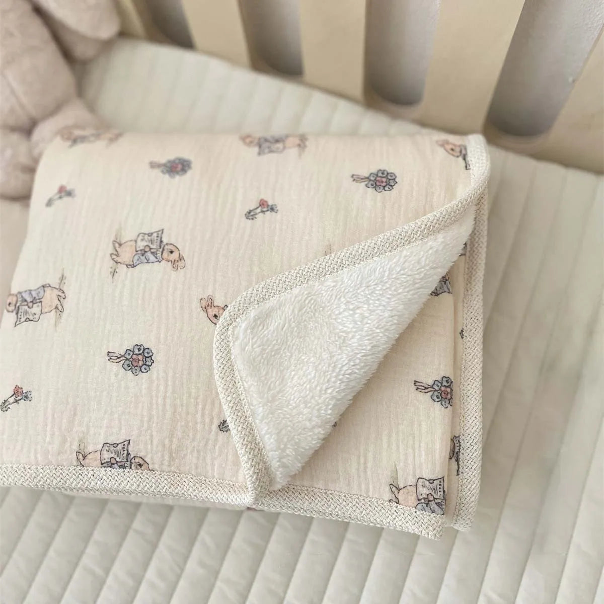 A light beige floral muslin baby blanket folded and displayed on a white surface.