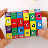 A hand holds a colorful Montessori math cube made of wooden blocks displaying numbers and arithmetic operations.